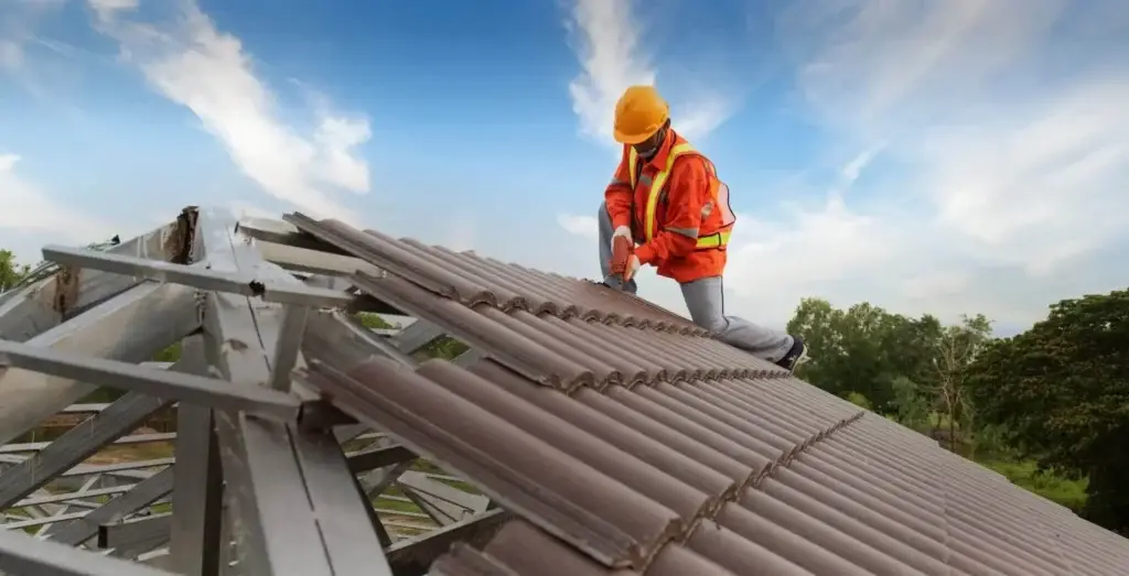 Roofing contractor wearing safety gear installing metal roofing on a residential structure.
