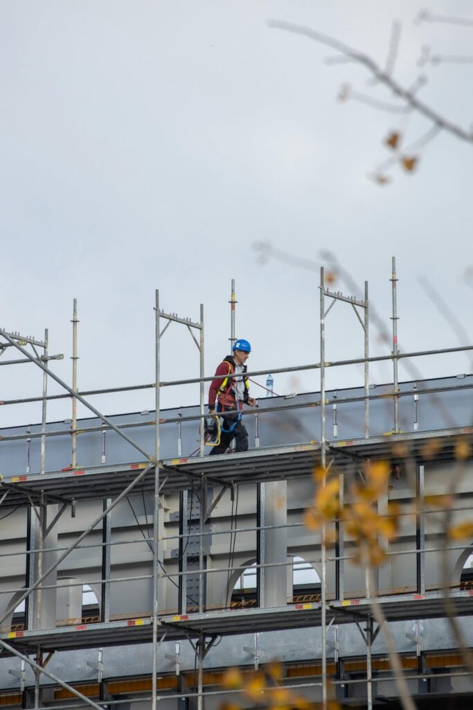Roofing contractor wearing safety gear working on scaffolding while installing or repairing a roof on a commercial building.